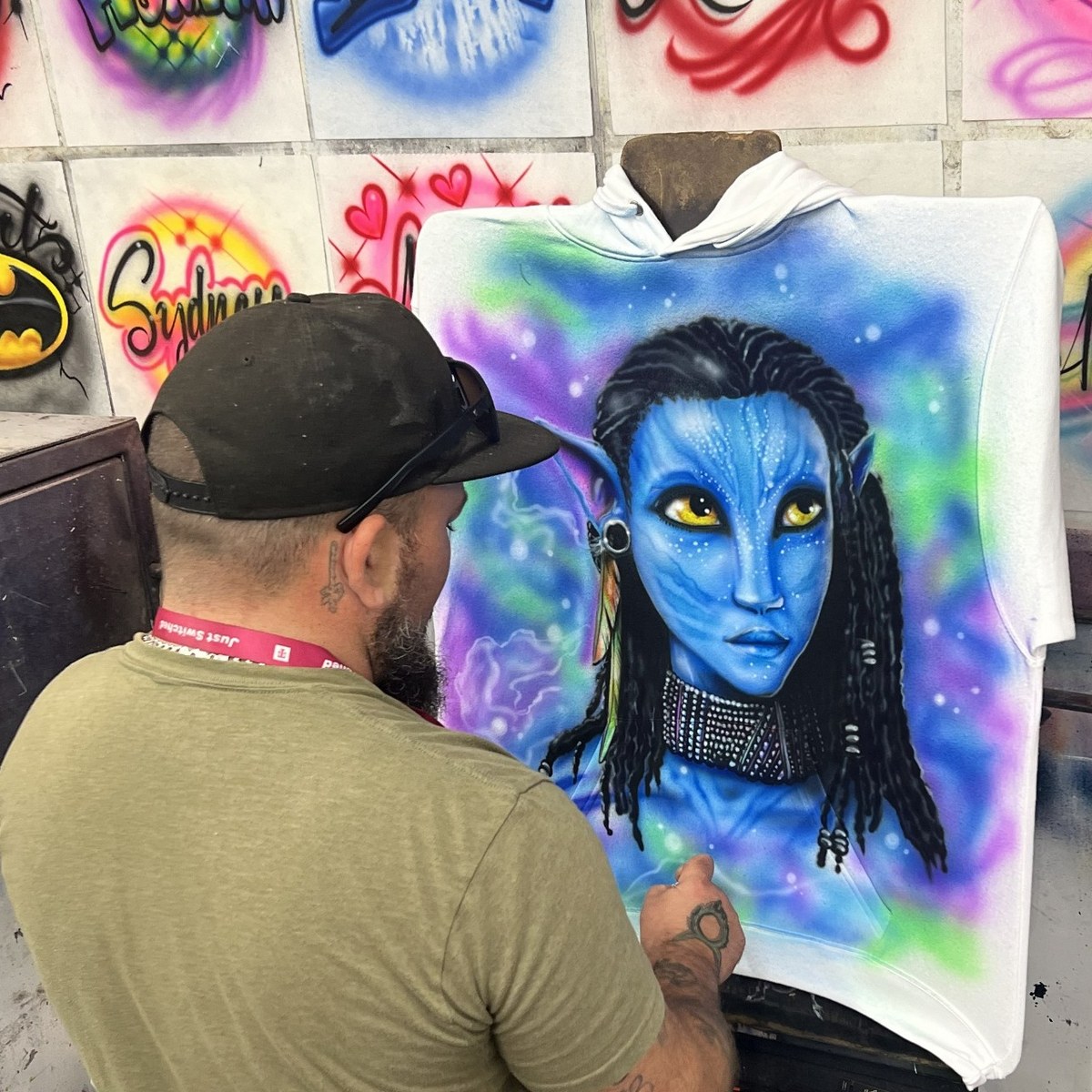 Sunshine Airbrush artist painting a detailed blue character on a custom hoodie