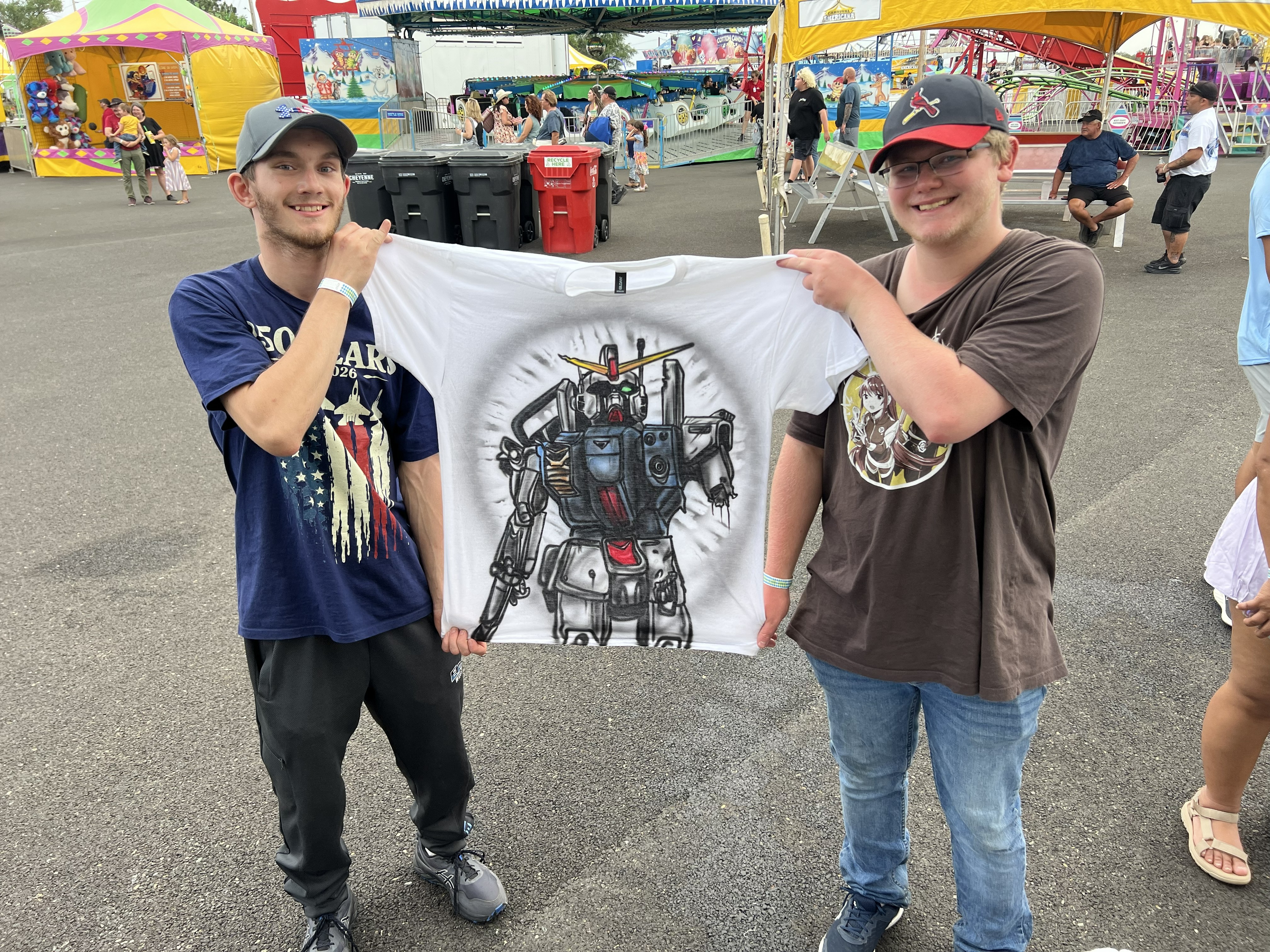 Two happy customers holding a custom airbrushed robot shirt at a fair